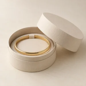 AI concept: round ivory bracelet box with a gold-coloured bangle, catalog view.
